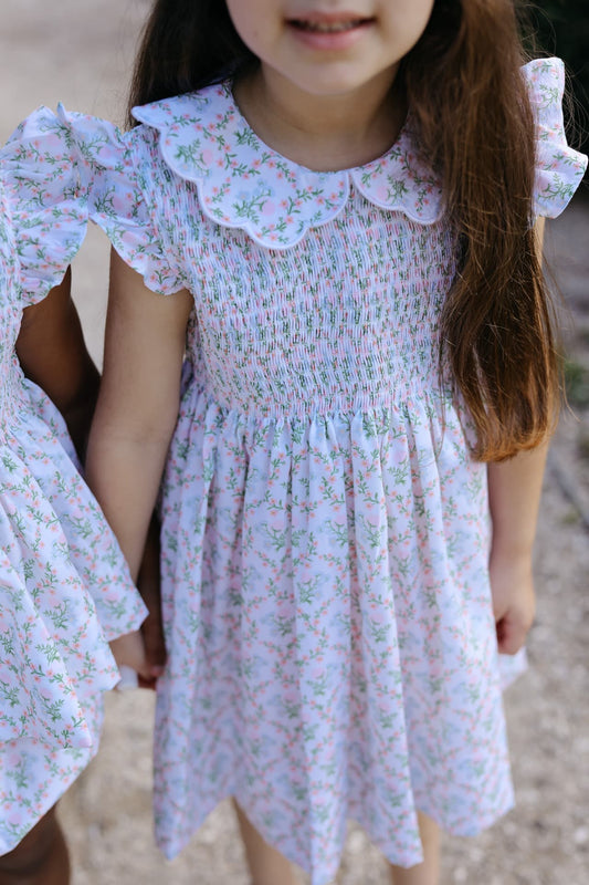 Child wearing a smocked floral dress with ruffled sleeves and scalloped collar.