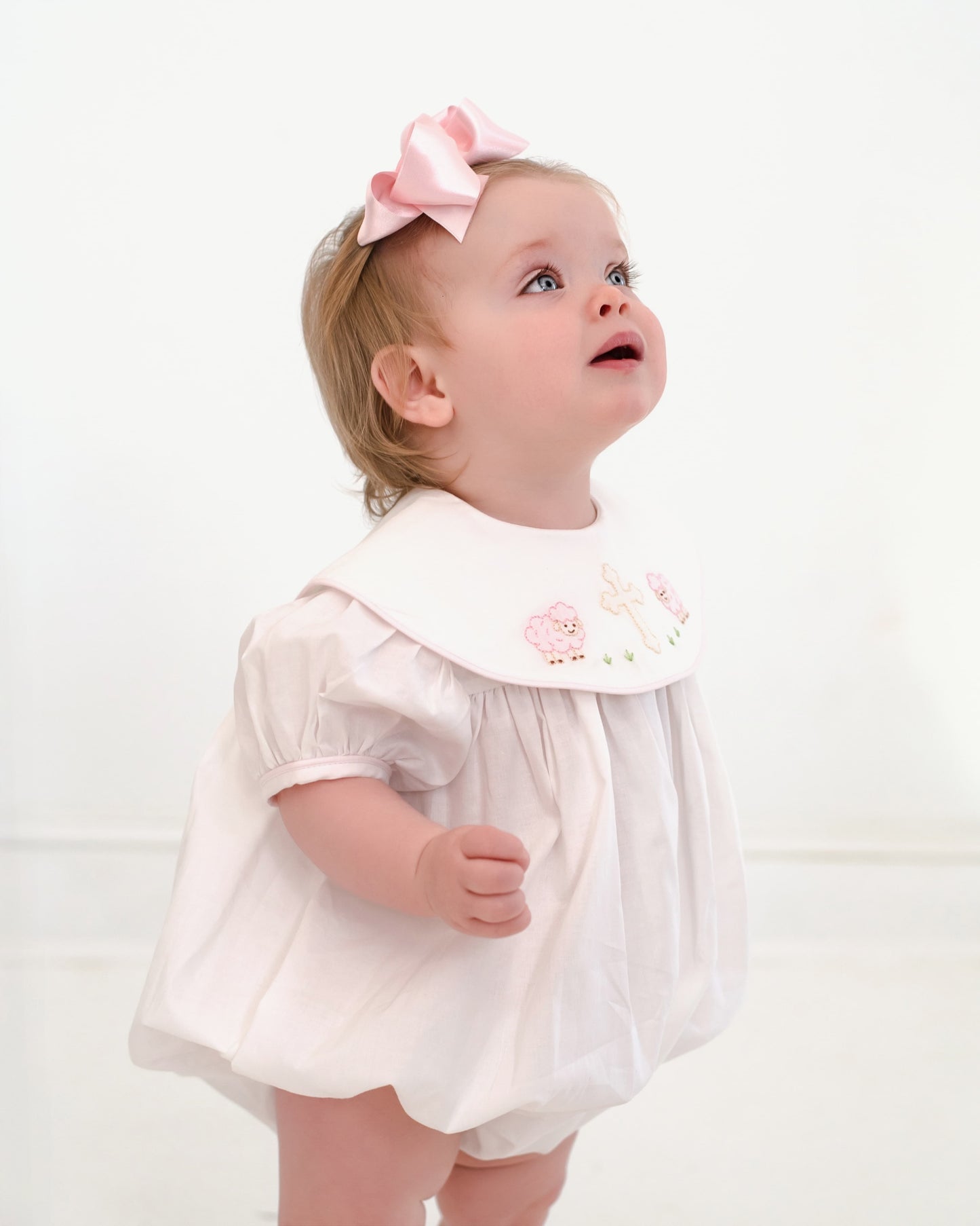 Child wearing a white dress with a pink bow on a white background
