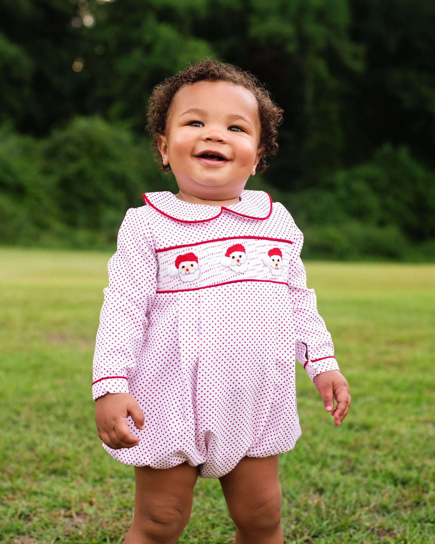 Child wearing a white dress with red trim and snowman design outdoors on grass