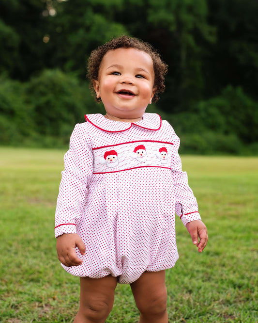 Child wearing a white dress with red trim and snowman design outdoors on grass