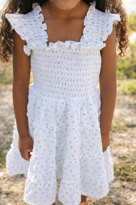 Child wearing a white dress with ruffled details, smocking and rosebuds in an outdoor setting