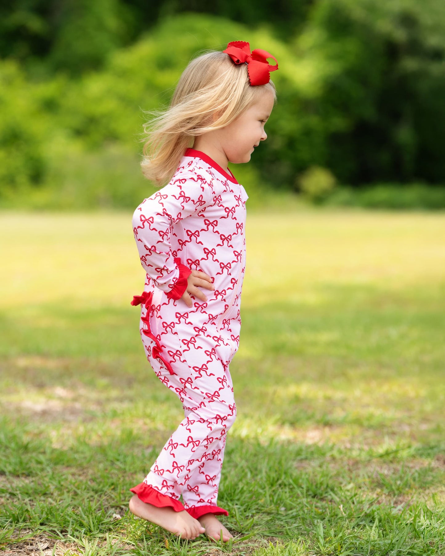 Child wearing a white outfit with red bows and trim outdoors on grass