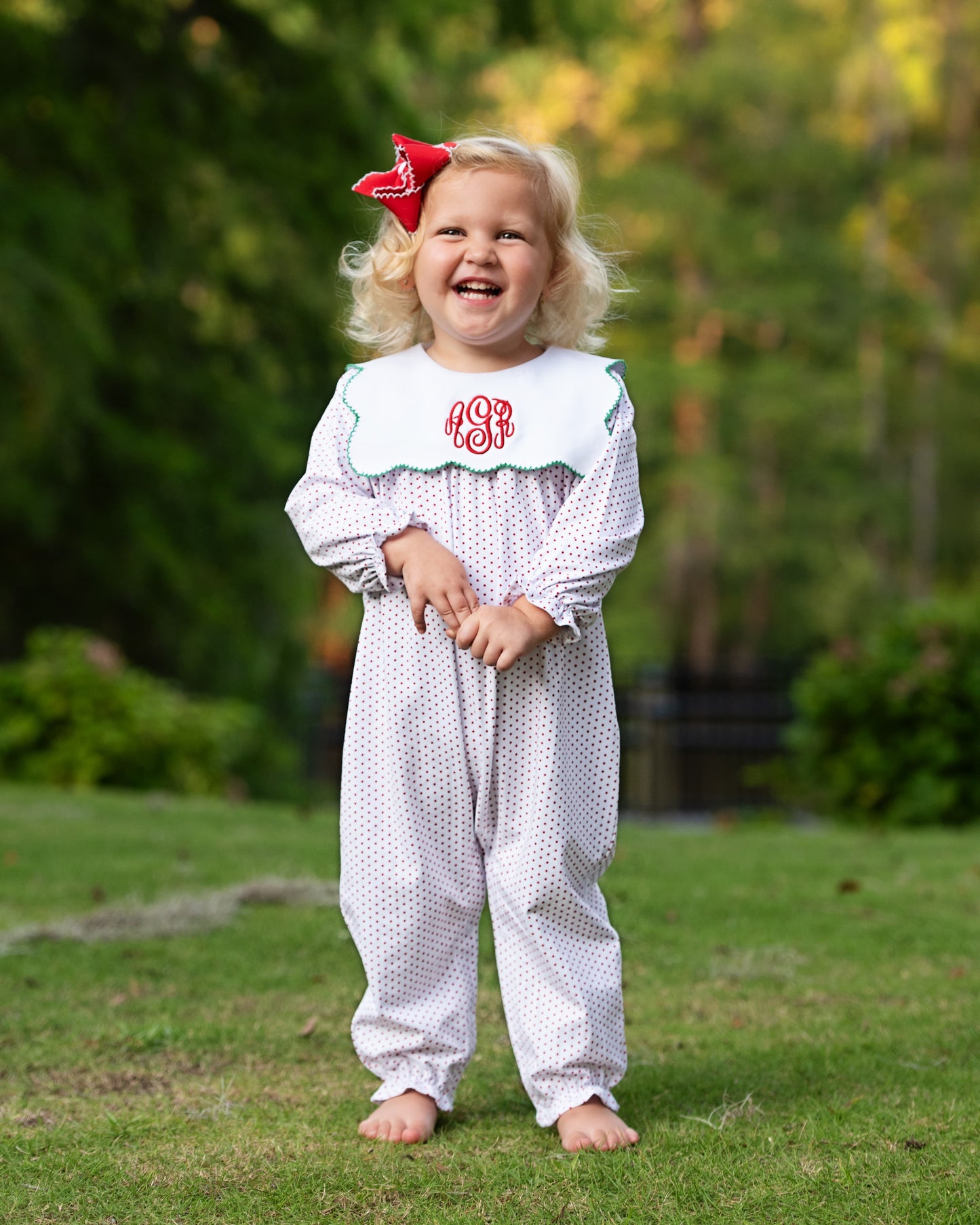 Child wearing a white patterned outfit with a red bow outdoors