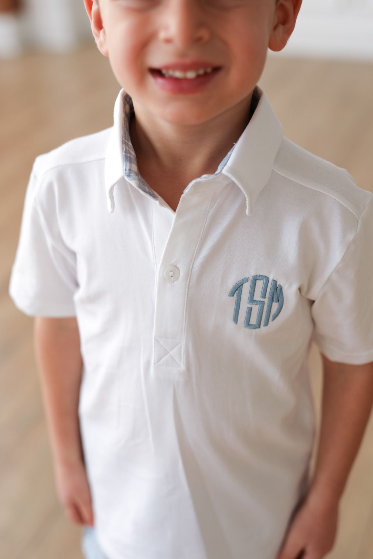 Child wearing a white shirt with blue monogram on a neutral background