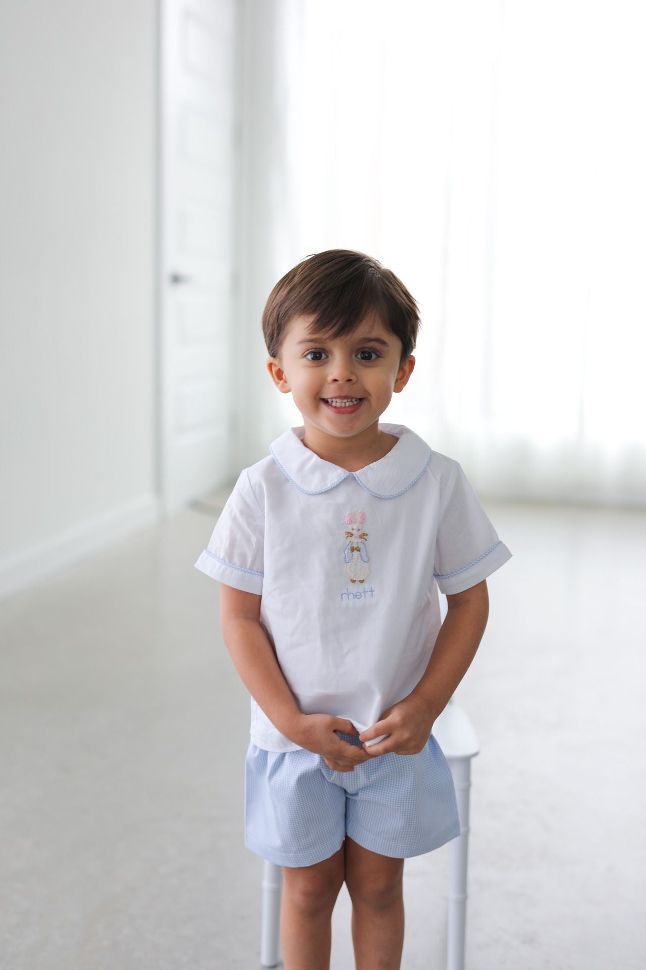Child wearing a white shirt with embroidery and light blue shorts on a white background