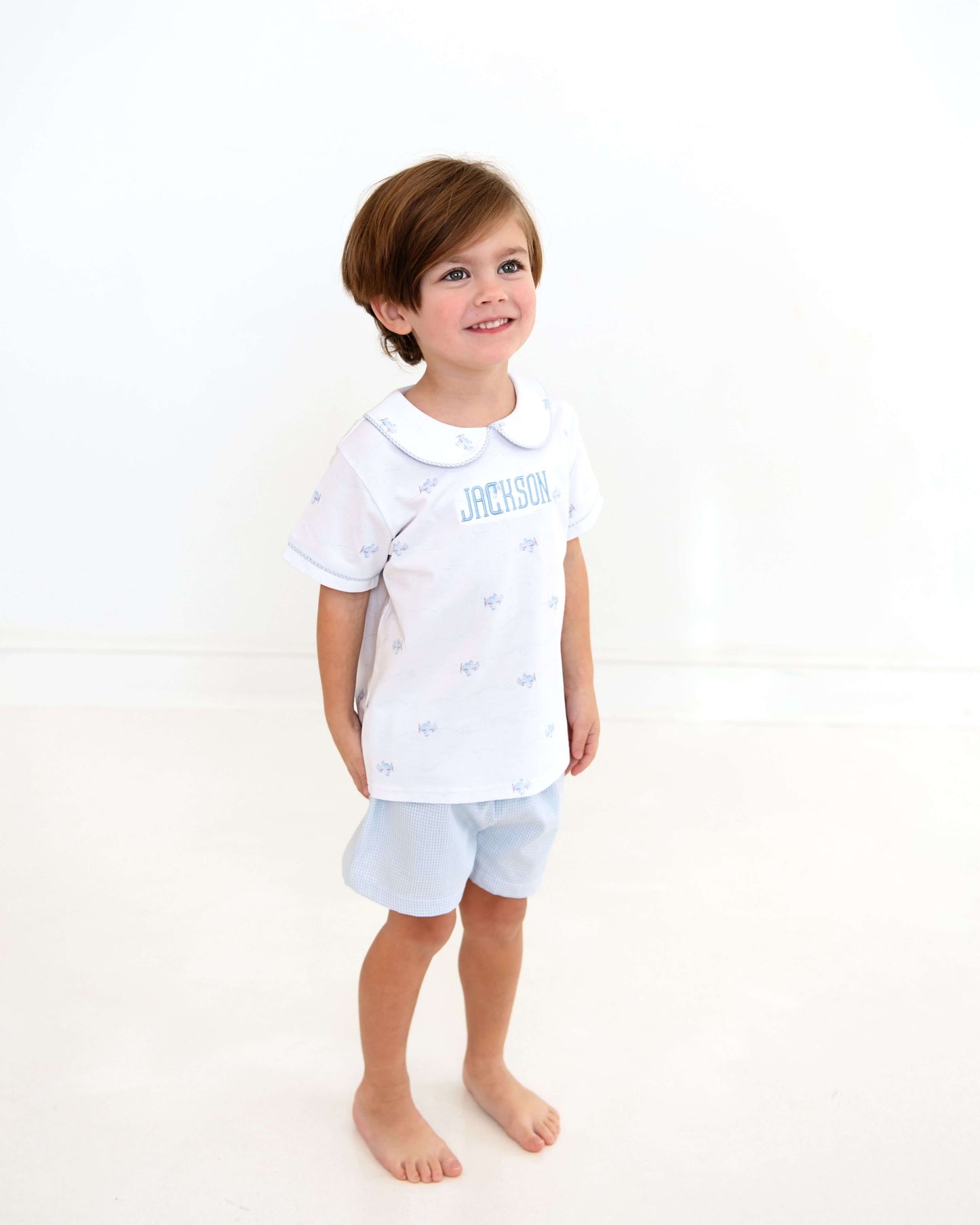 Child wearing a white shirt with text and light blue shorts on a white background