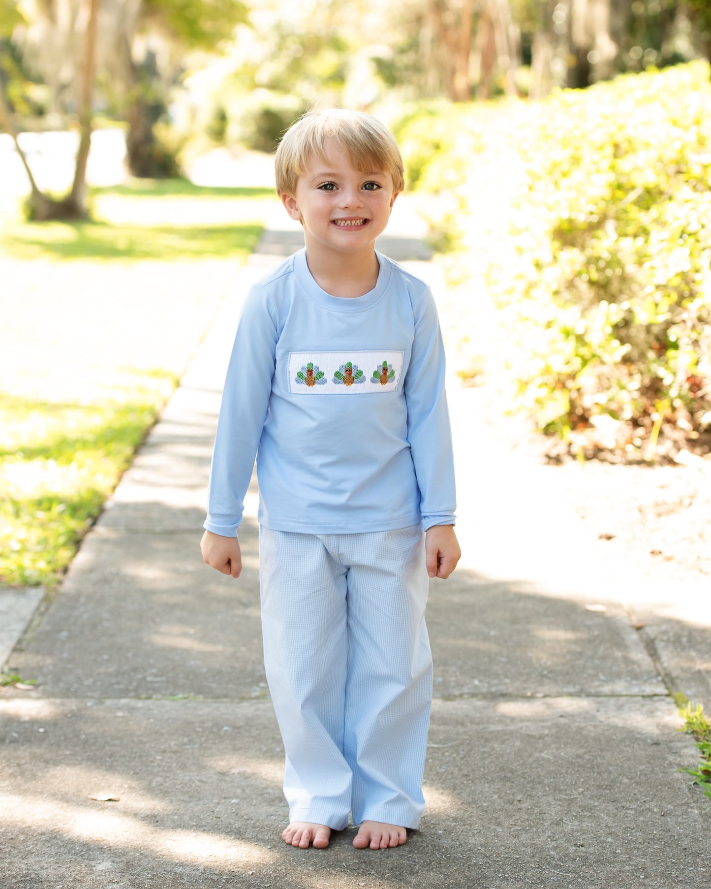Child wearing light blue pant set with a design of smocked turkeys on a path outdoors