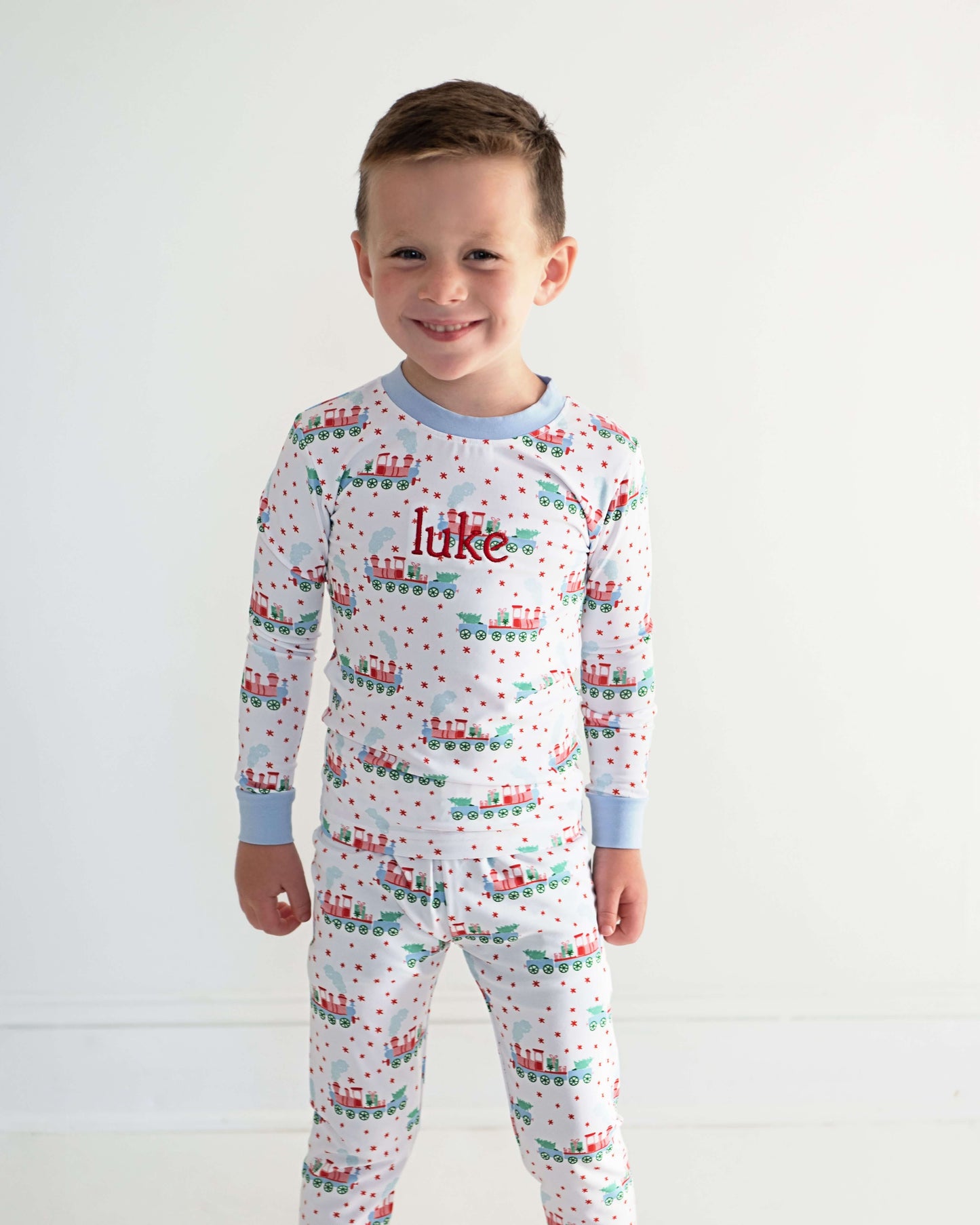 Child wearing pajamas with a train pattern and 'luke' printed on the chest against a white background