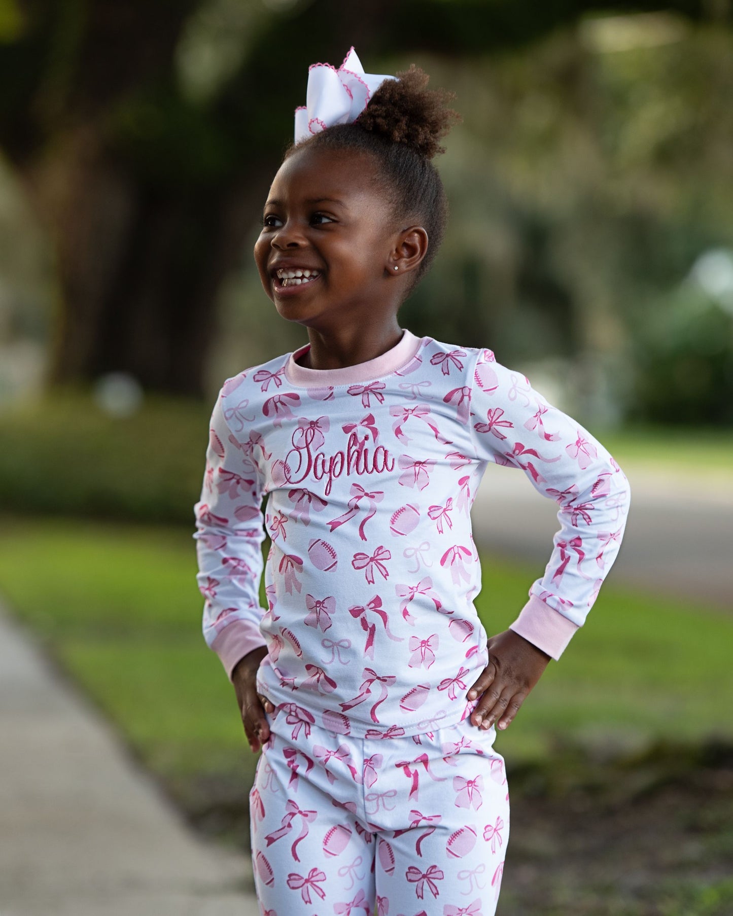 Child wearing pink and white pajamas with 'Sophia' printed on them, standing outdoors.