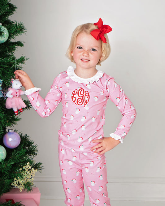 Child wearing pink heart-patterned pajamas with a red bow, standing next to a decorated Christmas tree.