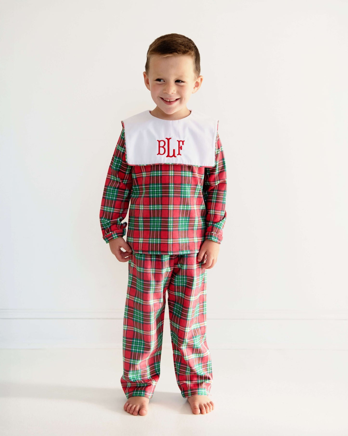 Child wearing red plaid pajamas with a white collar and 'BLF' monogram on a white background