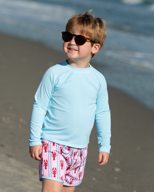 Child wearing sunglasses and a light blue shirt on a beach