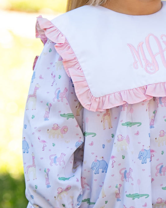 Children's dress with animal pattern and pink ruffled collar against a blurred outdoor background