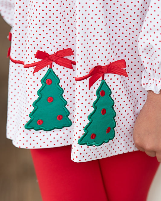 Close-up of a child's outfit with green Christmas tree decorations on a white shirt with red polka dots.