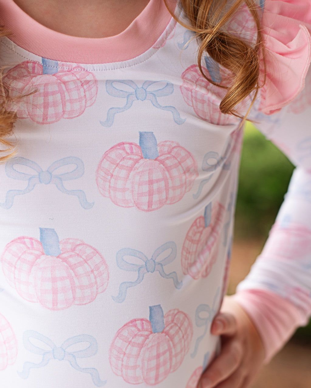 Close-up of a child's pajama set with pink pumpkins and blue bows pattern.
