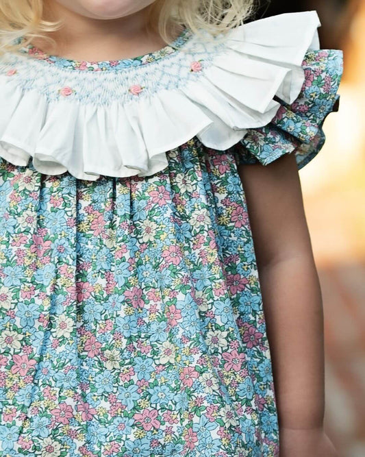 Close-up of a child wearing a floral dress with a white ruffled collar.