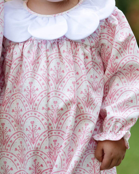 Close-up of a child wearing a pink and white patterned dress with a large white collar.