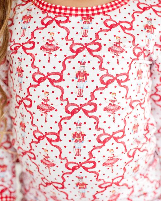 Close-up of a patterned fabric with red bows, polka dots, and Christmas-themed designs on a white background.