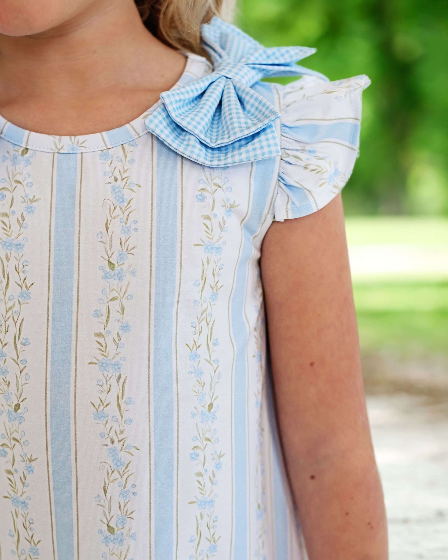 Close-up of a person wearing a light blue and white dress with floral patterns and a bow detail.