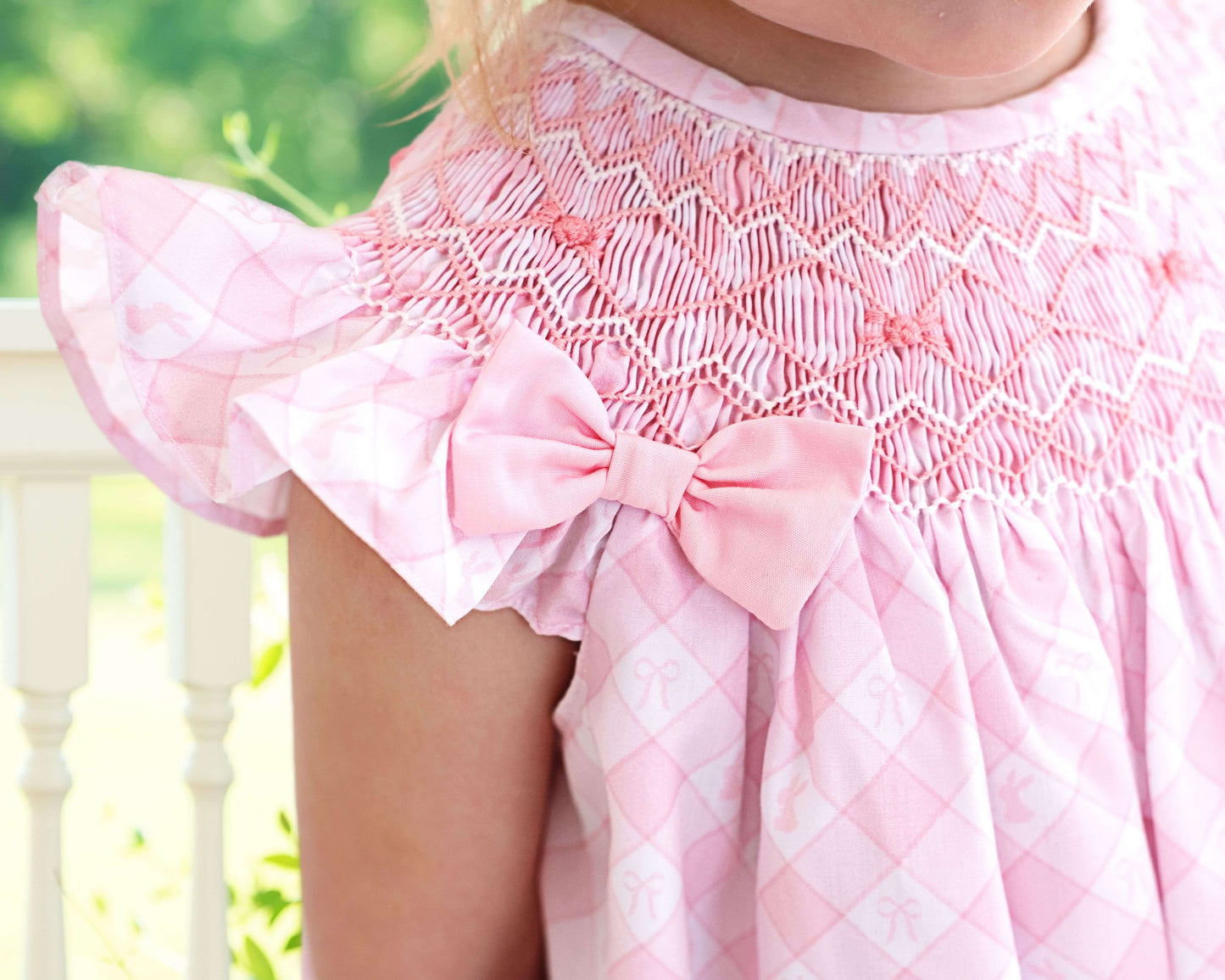 Close-up of a pink dress with a bow detail, blurred green background