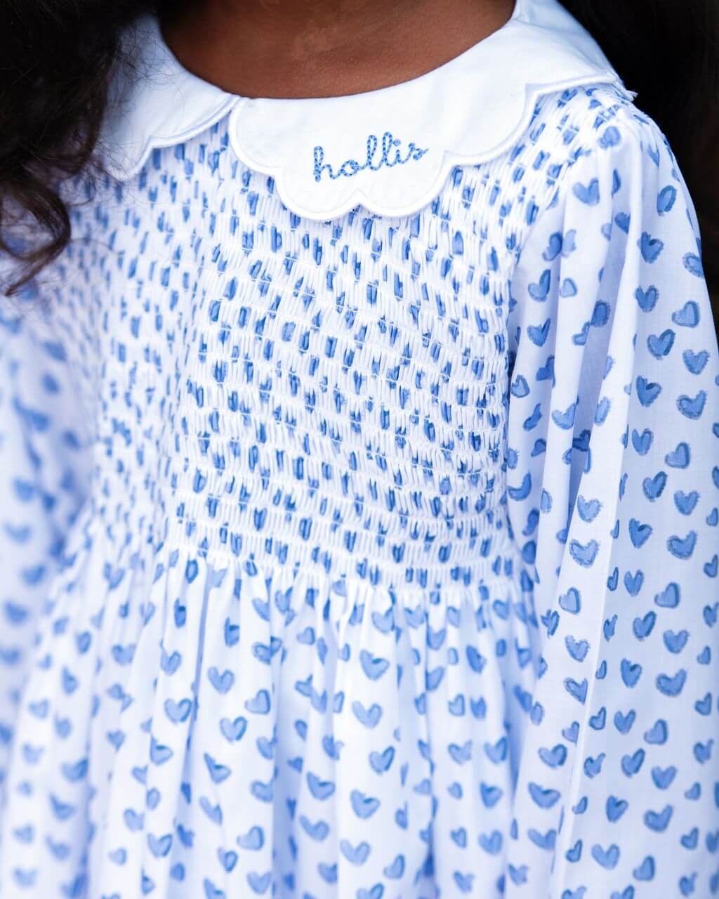 Close-up of a white dress with blue heart pattern and 'Hollis' branding.
