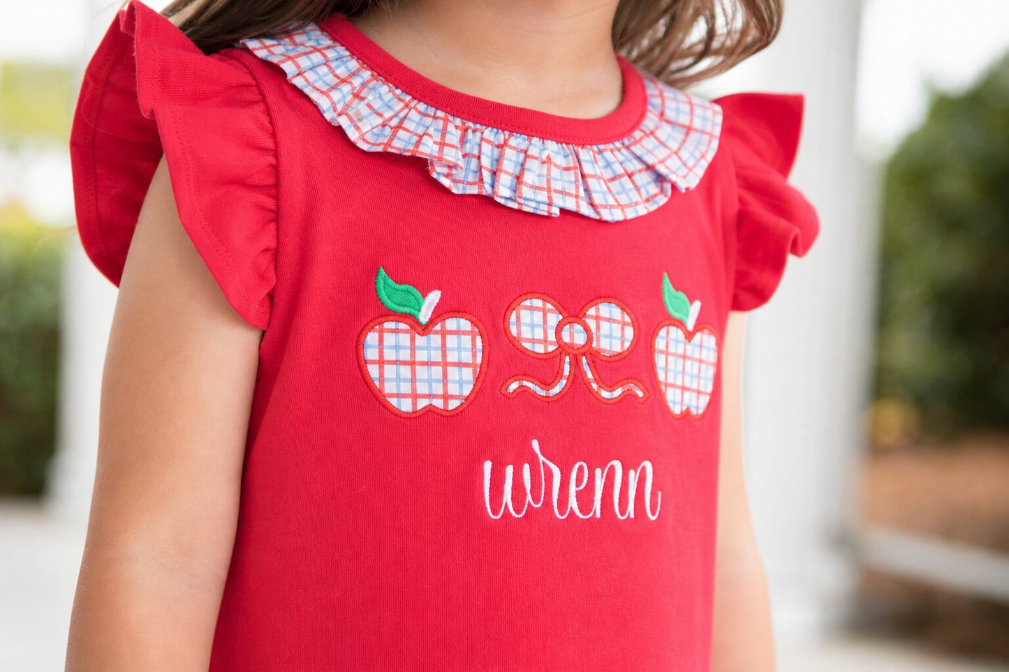 Closeup of a red shirt with applique apples and bow