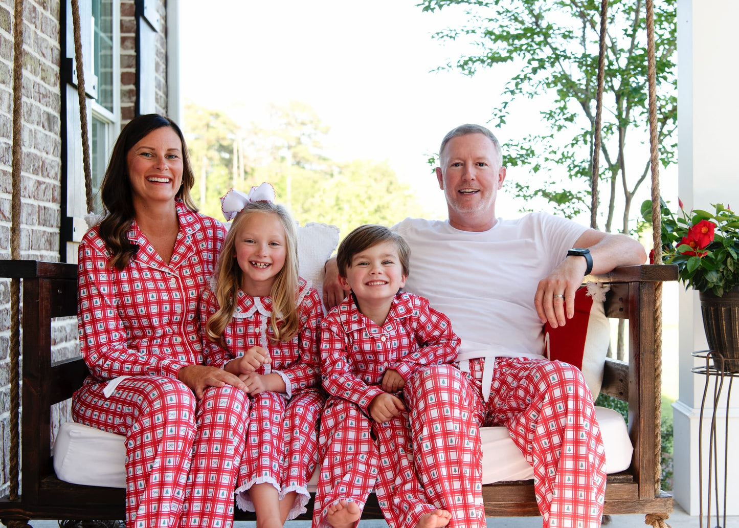 Family of four wearing red and white checkered pajamas sitting on a porch.