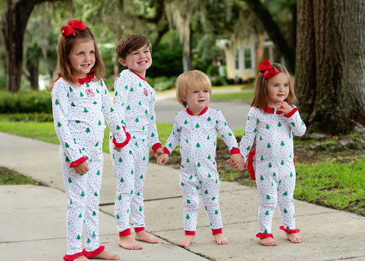 Four children in matching Christmas-themed pajamas standing outdoors on a sidewalk.