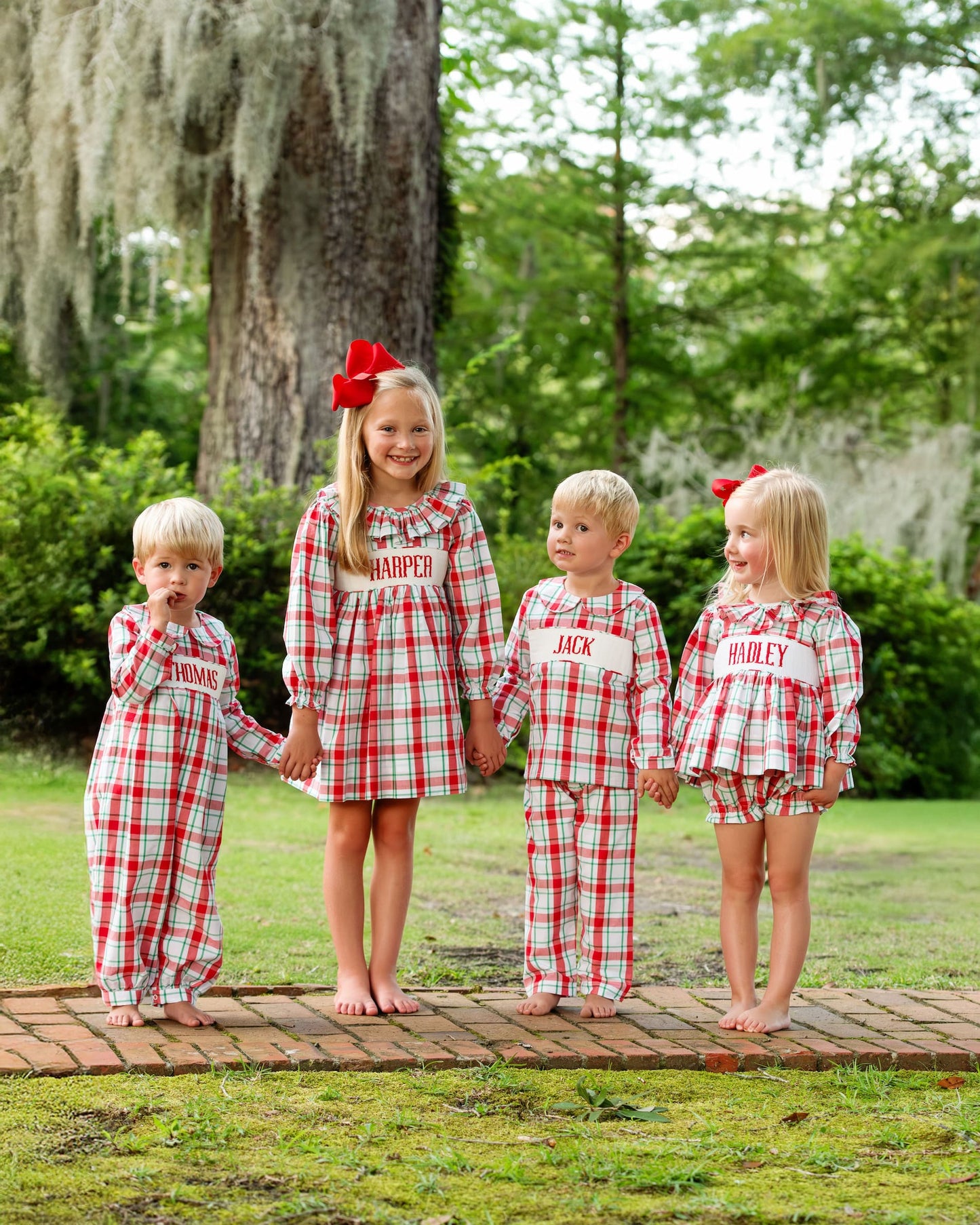 Four children in matching red and white checkered pajamas standing on a wooden platform outdoors.