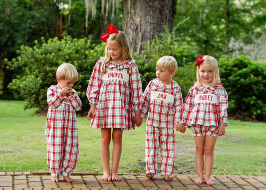 Four children in matching red and white plaid outfits with names on them, standing outdoors.