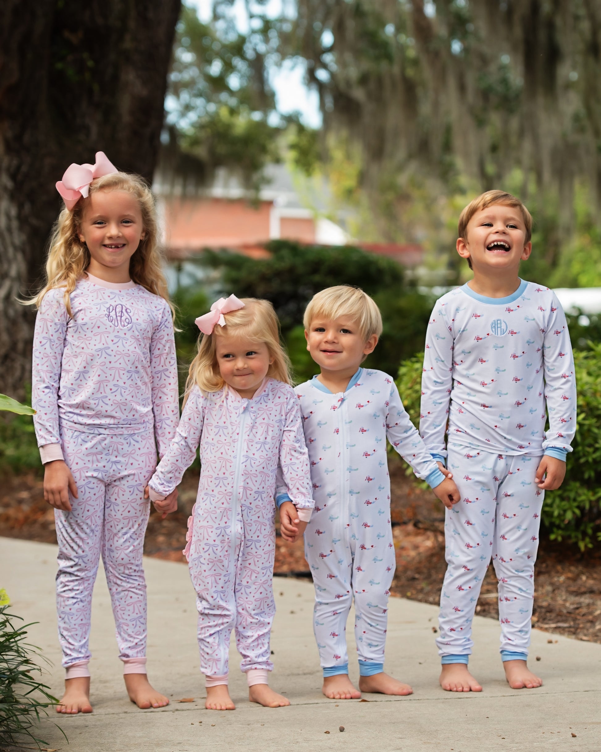 Four children wearing matching pajamas outdoors with trees in the background