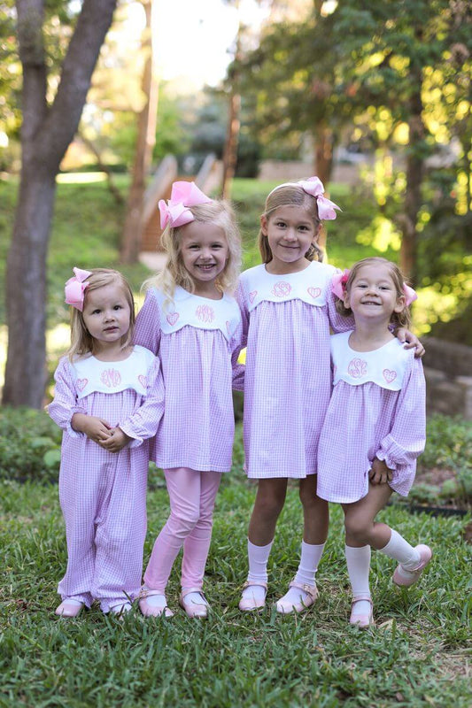 Four young girls in matching dresses standing outdoors with trees in the background