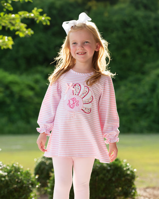 Girl standing outdoors wearing a pink outfit with a turkey applique on it