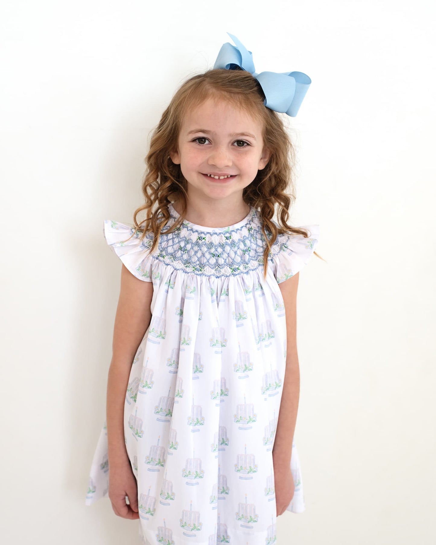 Girl wearing a cake print dress with smocking details on the neckline.