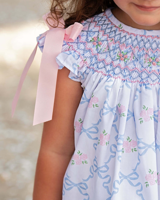 Girl wearing a dress with floral patterns and a pink ribbon.