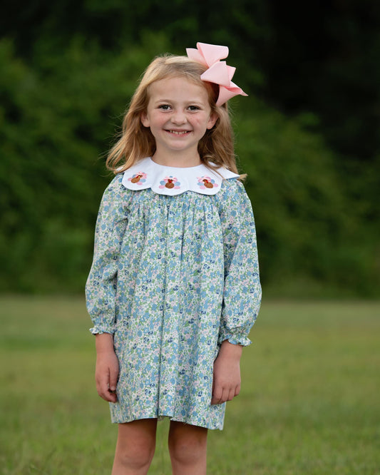 Girl wearing a floral dress with turkeys and pink bow standing on a field