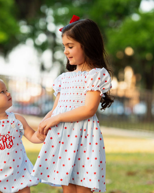 Girl wearing a star print dress holding a little girls hand.