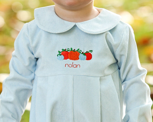 Light blue checkered dress with embroidered pumpkins and 'nolan' text, blurred outdoor background