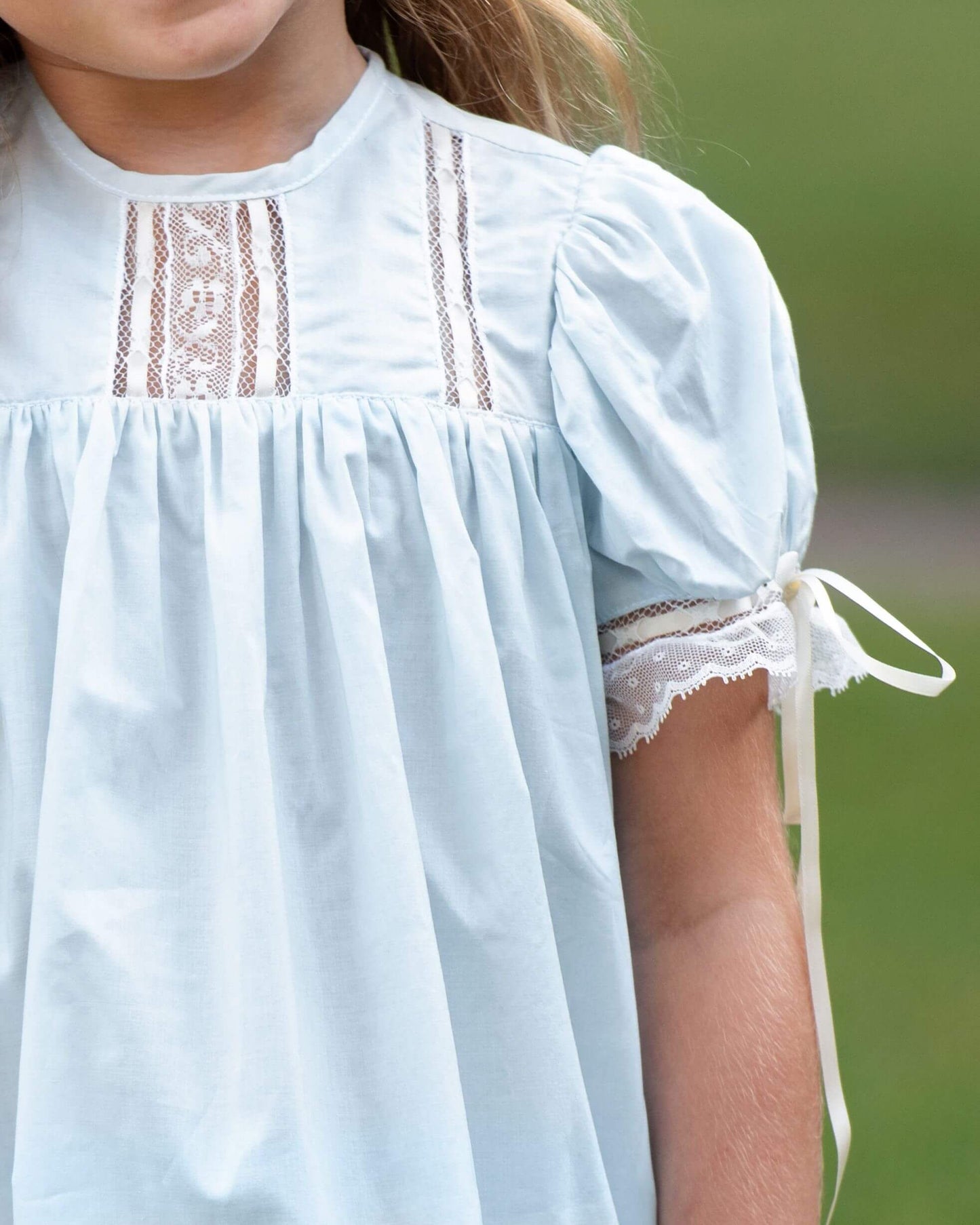 Light blue dress with lace details worn by a child against a blurred green background