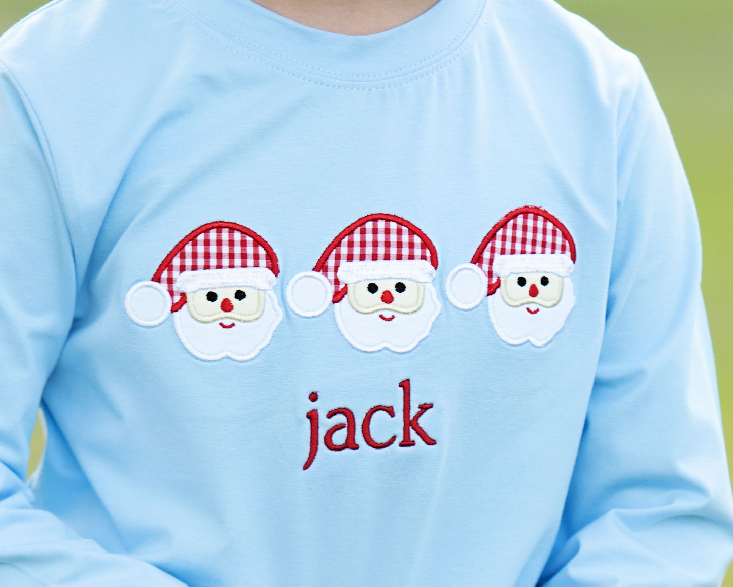 Light blue shirt with three cartoon Santa faces and the name 'jack' on a green background