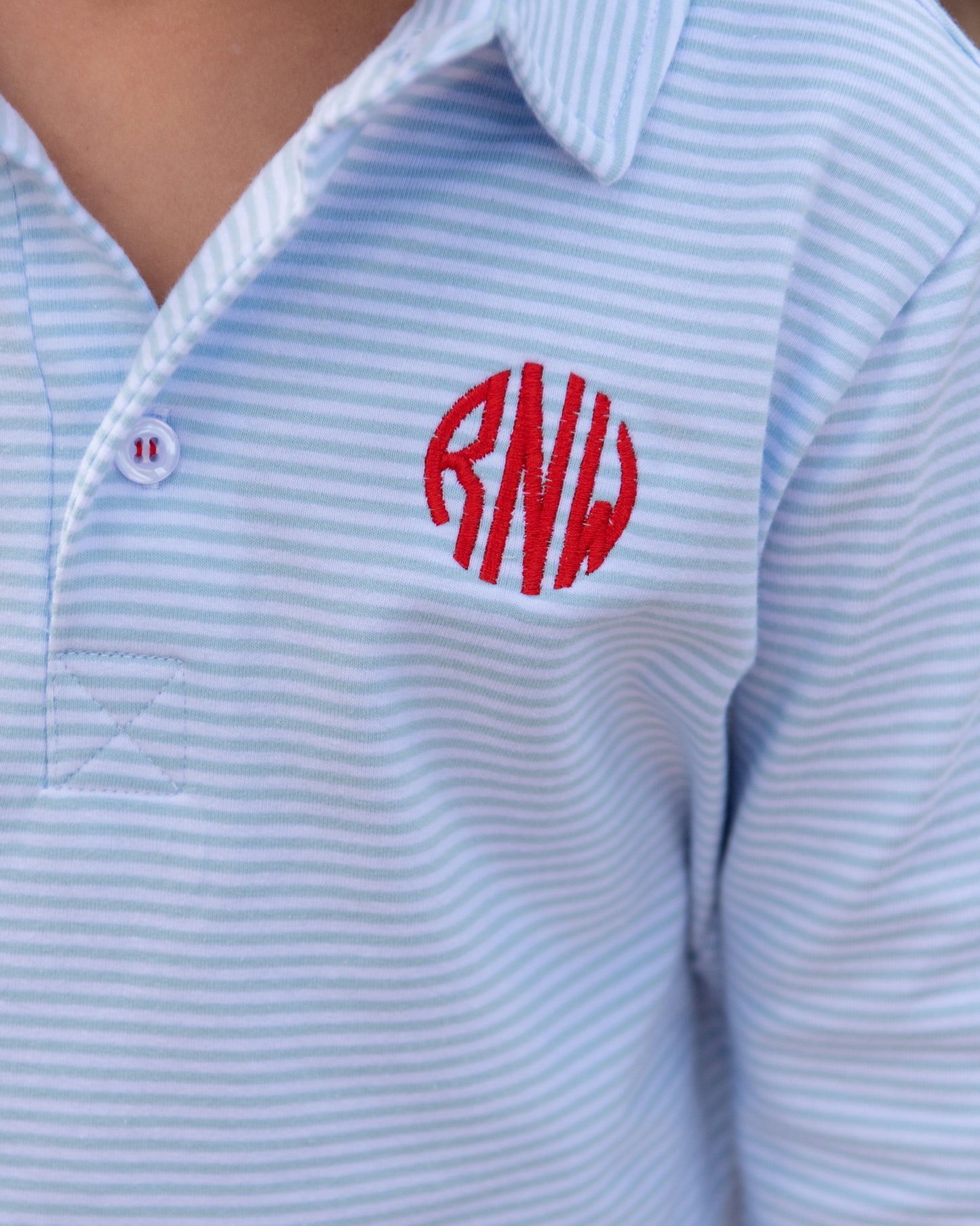 Light blue striped polo shirt with red monogram on a person wearing it.