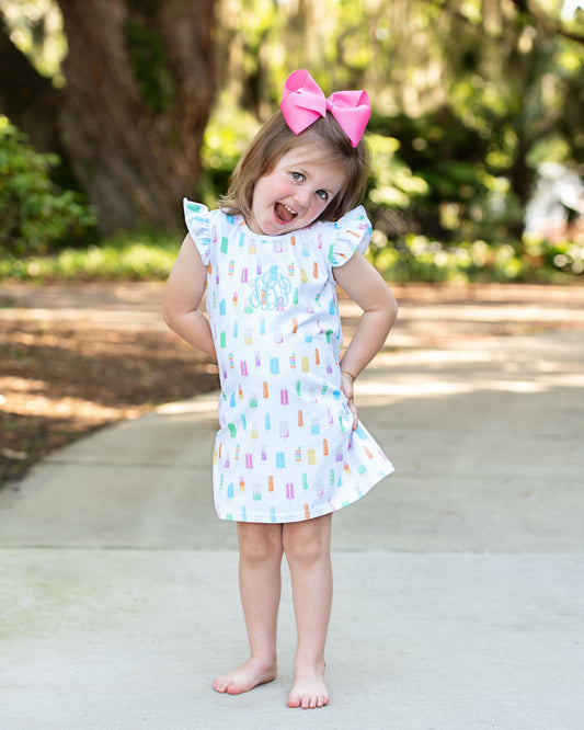 Little girl wearing a popsicle print dress outside with a pink bow in her hair