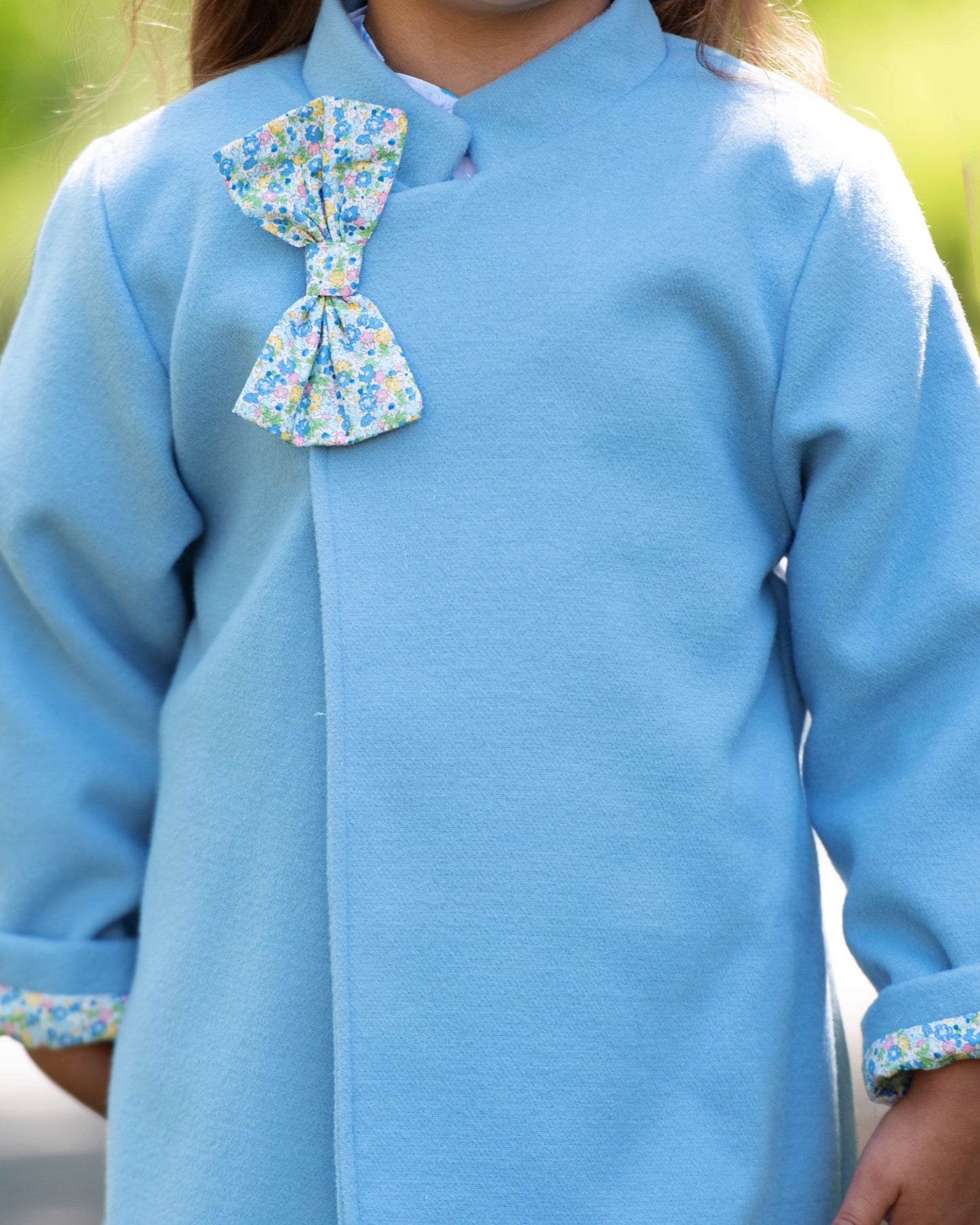 Person wearing a light blue dress with a floral bow detail on a blurred natural background