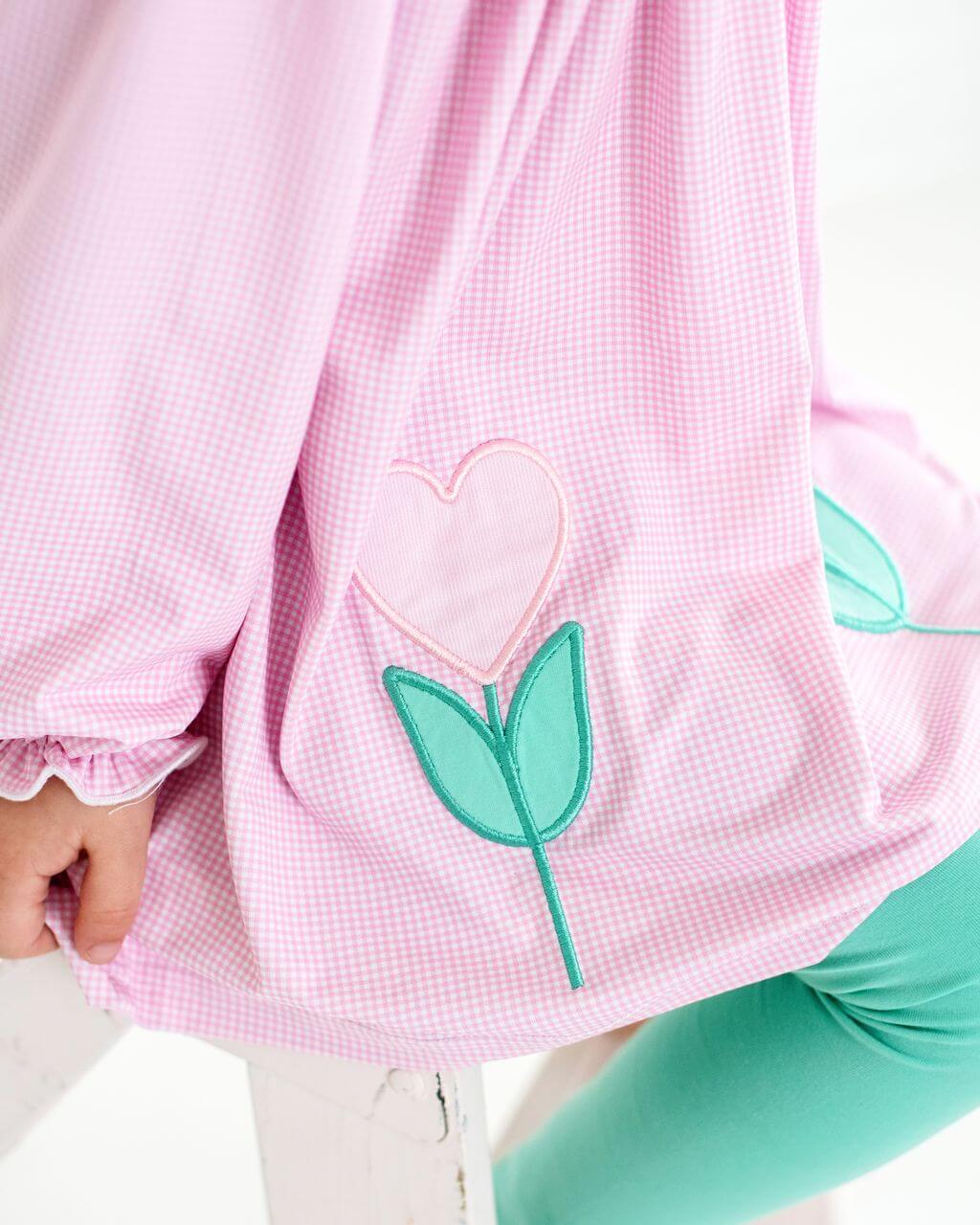 Pink checkered shirt with a heart and leaf design worn by a person.