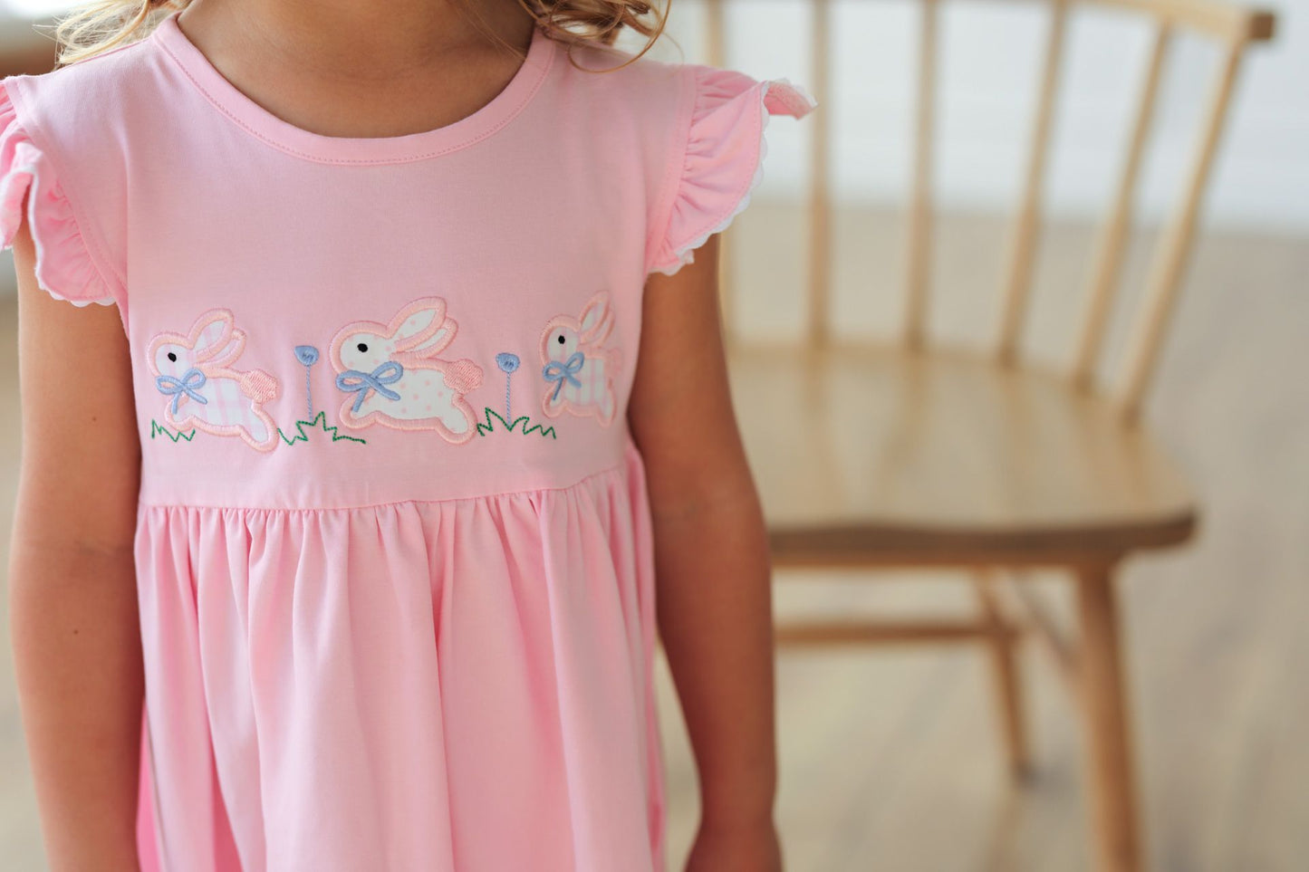 Pink dress with embroidered bunnies worn by a child, blurred background