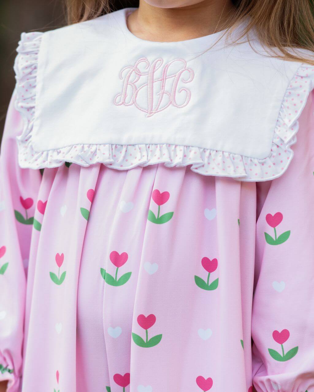 Pink dress with heart and flower pattern and white collar with embroidered initials.