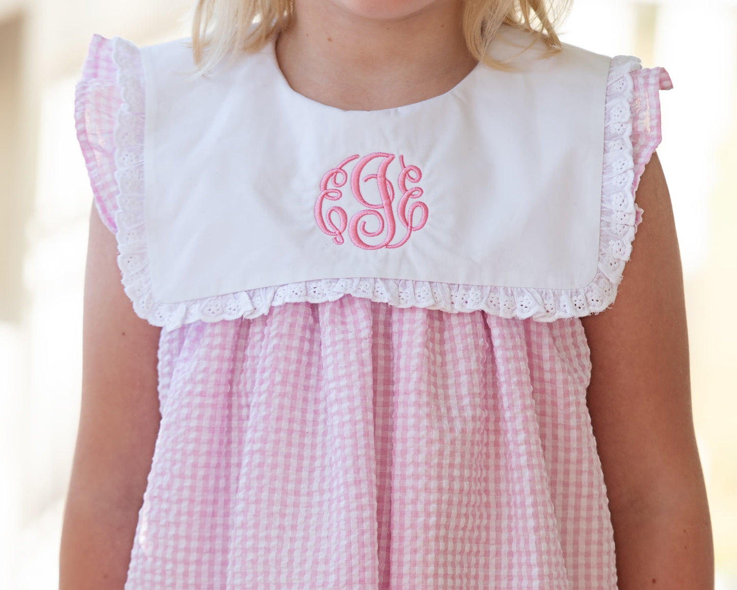 Pink seersucker dress with white collar and monogram on a blurred background