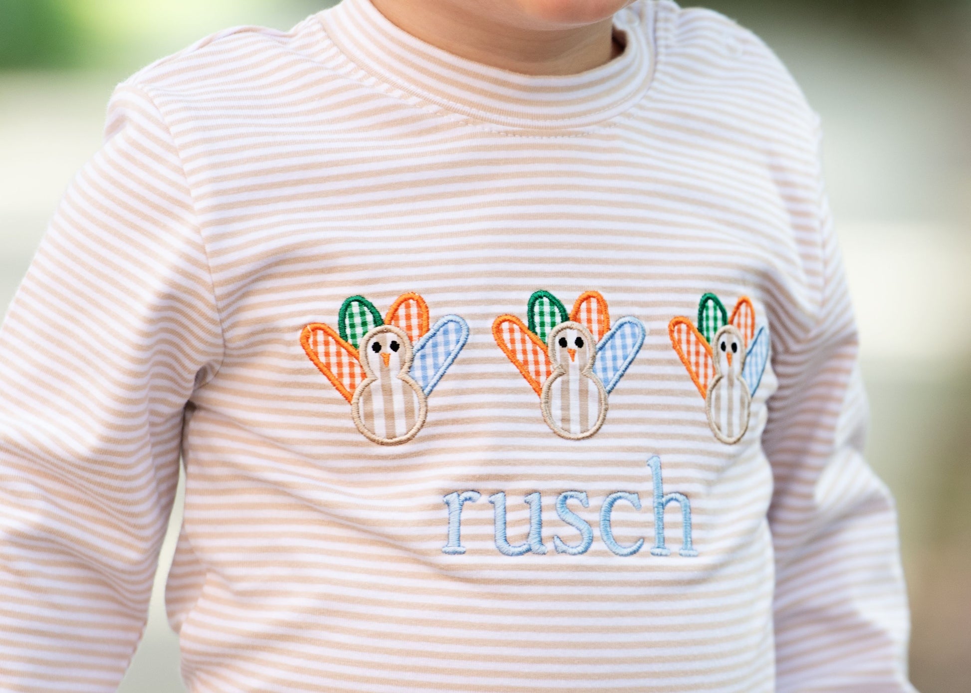 Close up of boy wearing a striped khaki with turkey appliqués and the name 'rusch' embroidered.