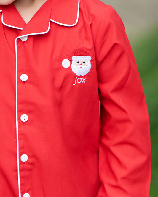 Red pajama top with a Santa face design and 'jax' text on a blurred green background