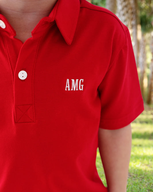 Red polo shirt with 'AMG' logo on a blurred outdoor background